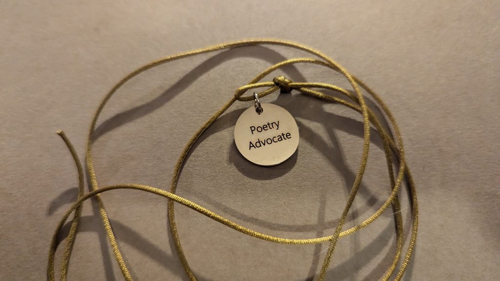 A golden cord, in a pile, to which is attached a gold medallion, on which is inscribed the words "Poetry Advocate".