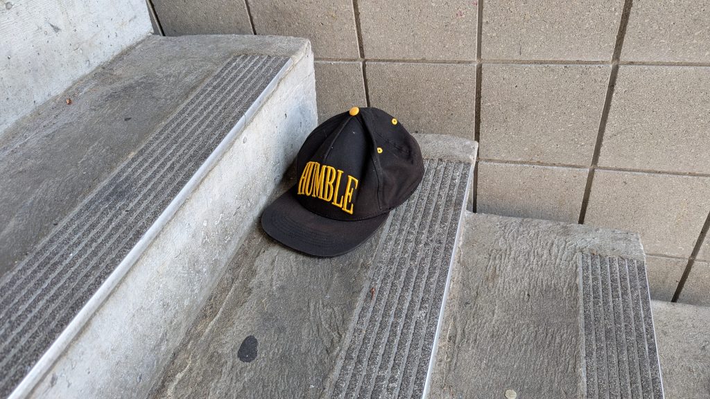An abandoned trucker hat in a concrete stairwell. The hat is black, with the word HUMBLE embroidered in yellow.